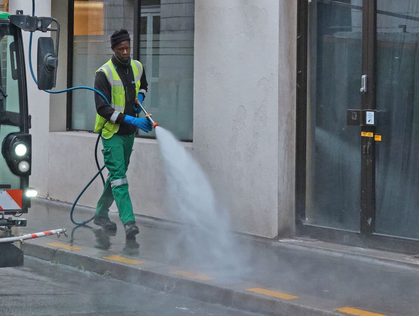 Crew member in safety gear pressure washing a street
