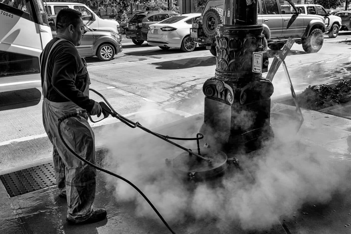 Technician steam pressure washing a city sidewalk