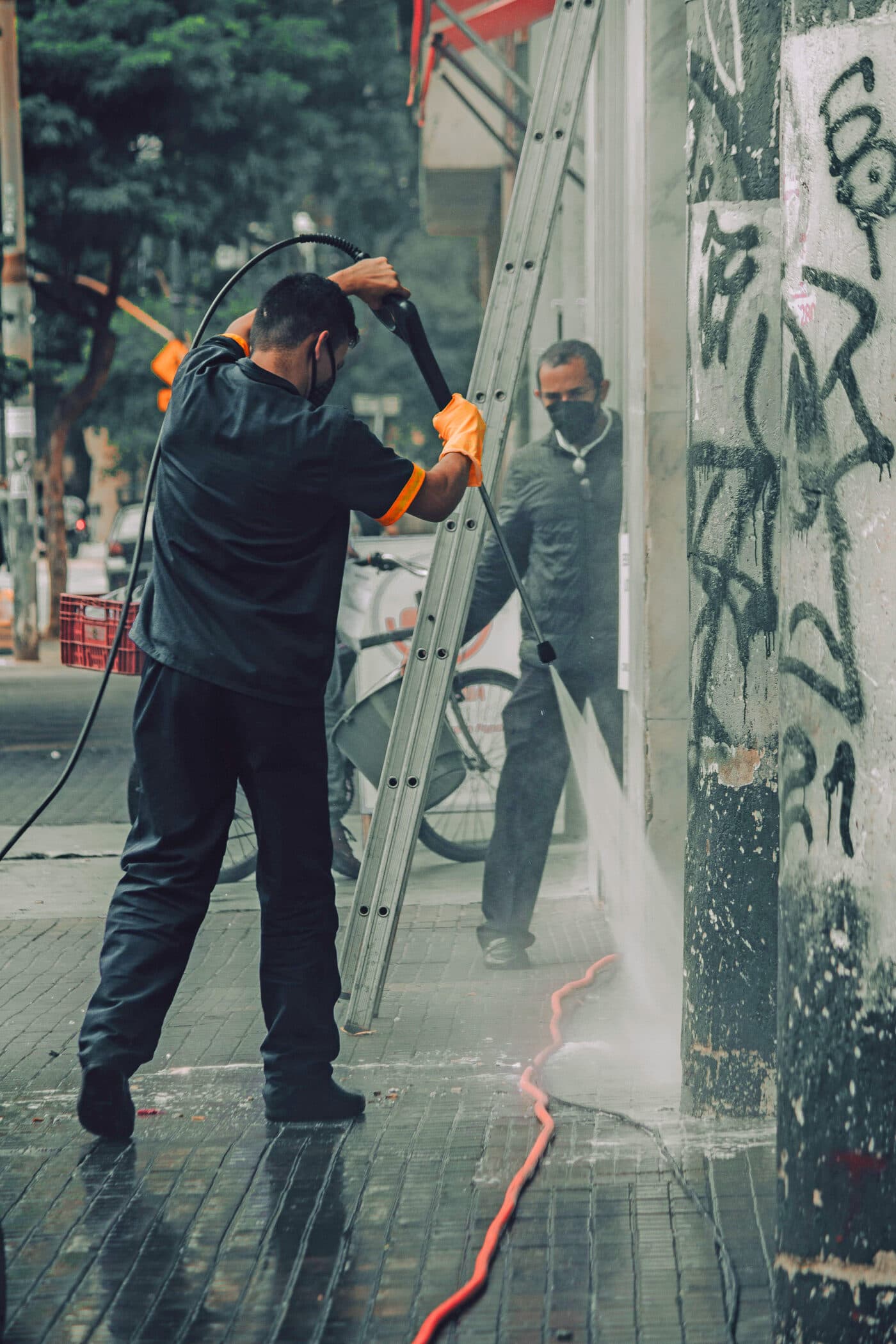 Worker removing graffiti from a wall with pressure washing equipment